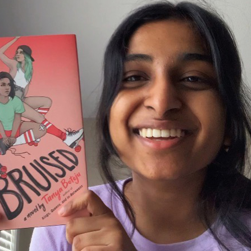 Photo of a smiling teenager holding up a young adult novel.